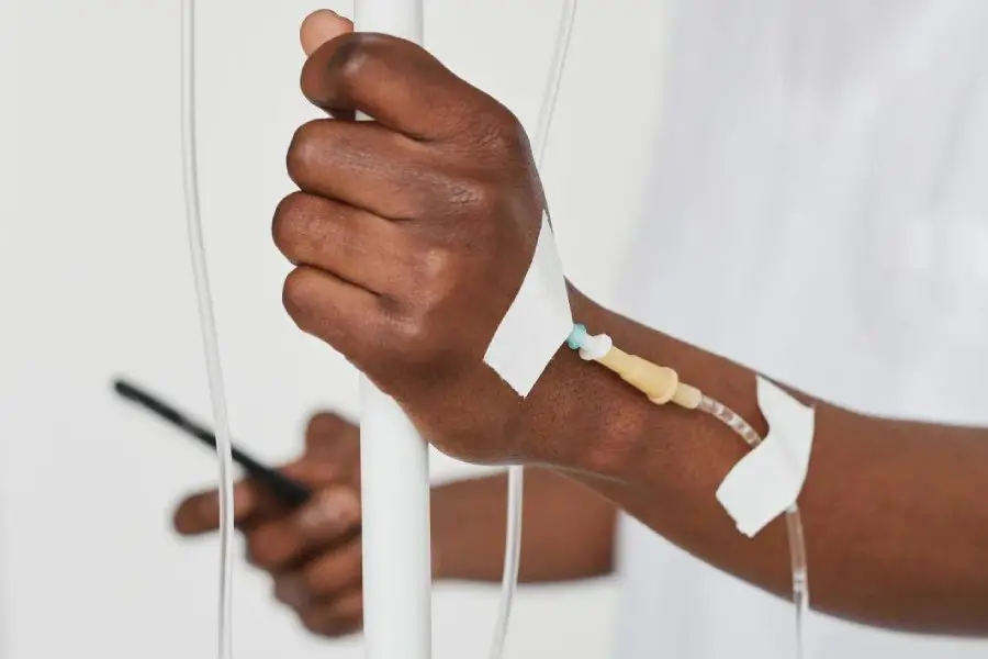 Person holding unto a white metal stand with an IV inserted in their arm