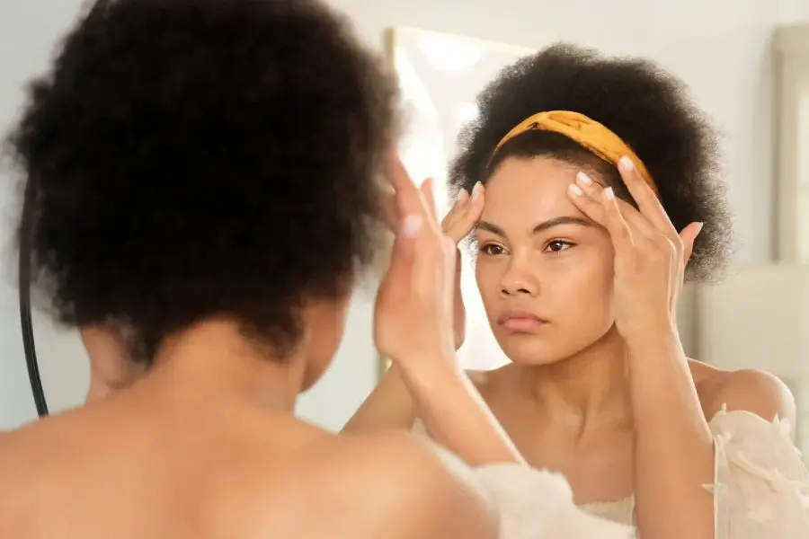 Woman with an afro wearing a yellow headband checking her forehead