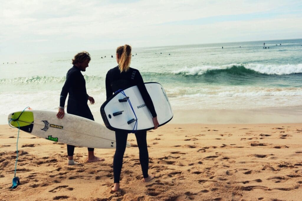 A Couple in Scuba Suits Holding a Surf Board