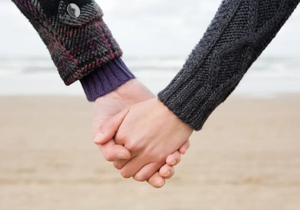 The holding hands of two people wearing long-sleeved tops